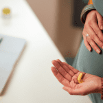 Pregnant woman standing by laptop and holding vitamins