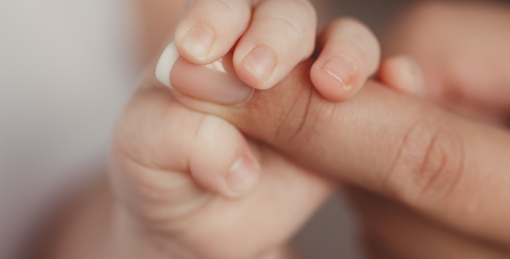 Newborn baby grabbing onto moms fingers